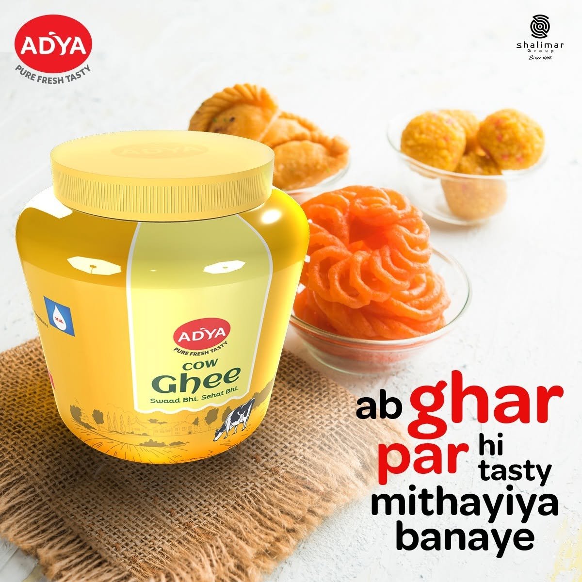Adya Dairy Cow Ghee product advertisement featuring traditional Indian sweets, including jalebi and laddoo, with a large ghee jar.